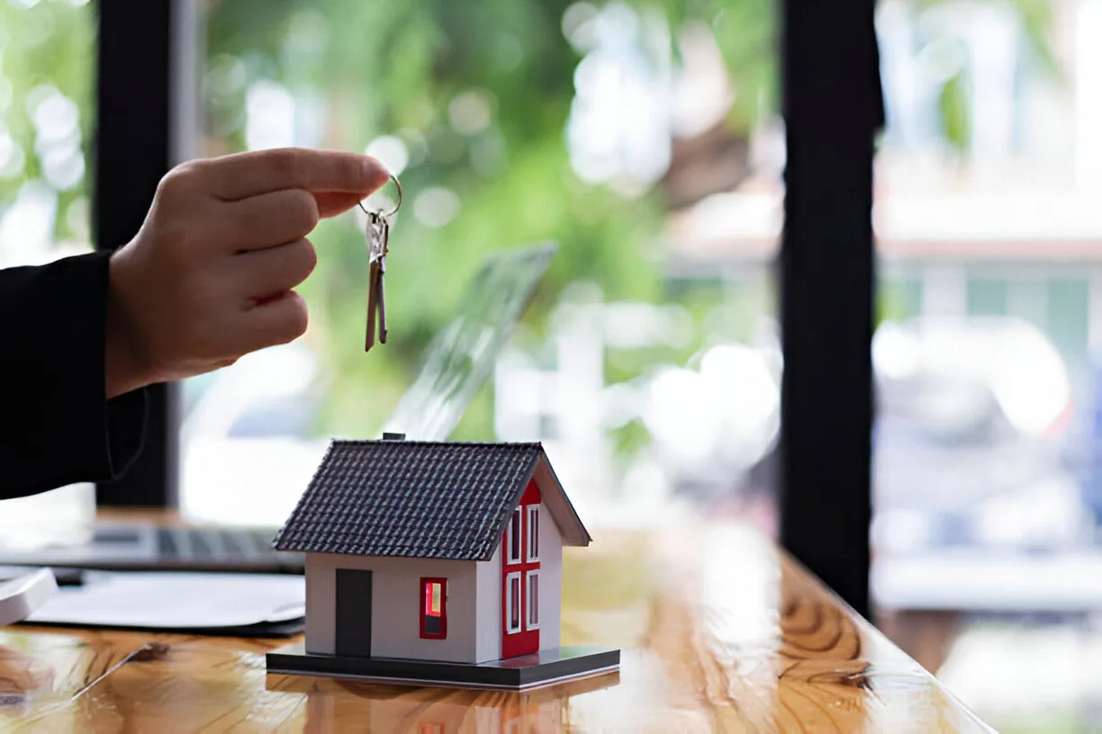 A set of keys held over a model house on a desk