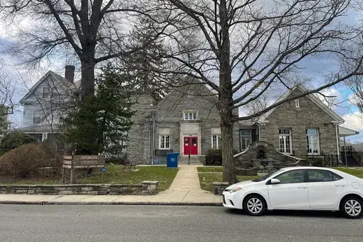 Stone library building with red doors, lawn, trees and parked white car., Ardmore, Pennsylvania