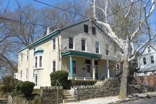 Two-story stucco house with porch and large tree on a residential street., Darby, Pennsylvania