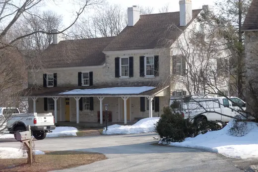 Two-story stone house with porch, snow on ground and parked vehicles, East Whiteland Township, Pennsylvania