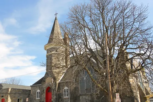 Stone church with red doors and a large leafless tree in front, Eddystone, Pennsylvania