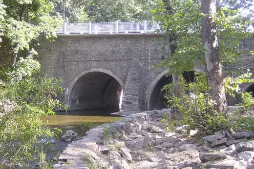 Stone arch bridge over a shallow river with rocky riverside and trees, Frankford, Pennsylvania