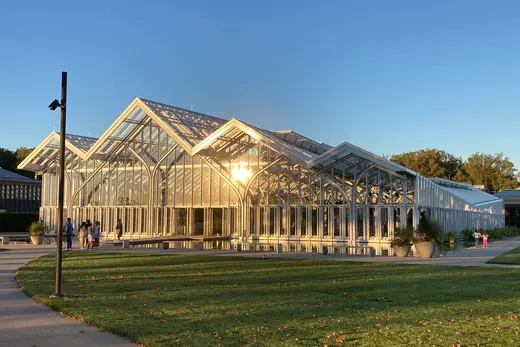 Glass conservatory building reflecting sunset beside lawn and pathway., Kennett Square, Pennsylvania