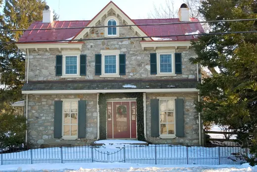 Stone two-story house with red roof and snow-covered yard., Lionville, Pennsylvania