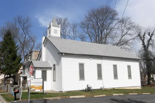 Small white church building with steeple beside a street and parked area, Nether Providence Township, Pennsylvania