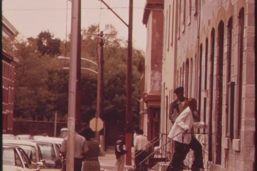 Urban sidewalk with medical center sign and people on rowhouse steps, North Philadelphia, Pennsylvania