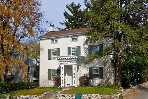 Two-story house with green shutters and front porch by stone wall., Plymouth Meeting, Pennsylvania
