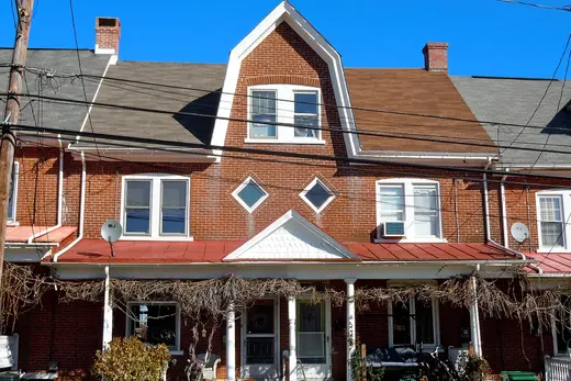 Brick rowhouse with front porch and dormer under clear blue sky., Red Hill, Pennsylvania