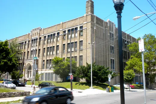 Large brick school building beside a busy street with passing cars., Roxborough, Pennsylvania