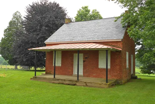 Small red-brick house with front porch on grassy lawn and large trees., Upper Oxford Township, Pennsylvania