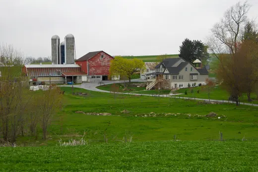 Farmhouse and red barn with silos on green rolling farmland, West Sadsbury Township, Pennsylvania